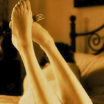 Sexy young woman lying on a bed. She is holding a fork carefully and casually between her feet.